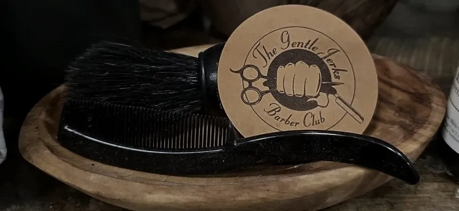 A leather Gentle Jerks Barber Club coaster beside a comb and a barber brush