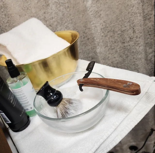 Straight razor, shaving brush and a warm towel laid out on a tray